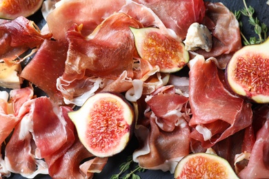 Delicious ripe figs and prosciutto served on black table, flat lay