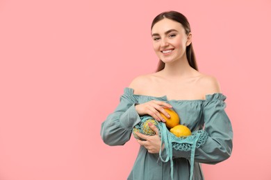 Woman with string bag of fresh lemons on pink background, space for text