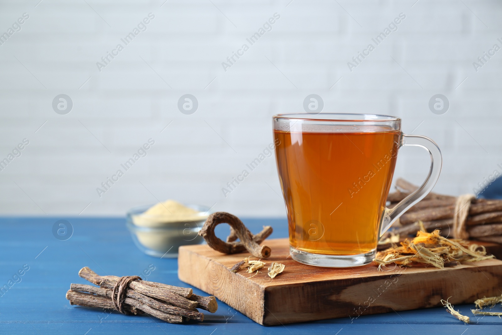 Photo of Aromatic licorice tea in cup and dried sticks of licorice root on blue wooden table, space for text