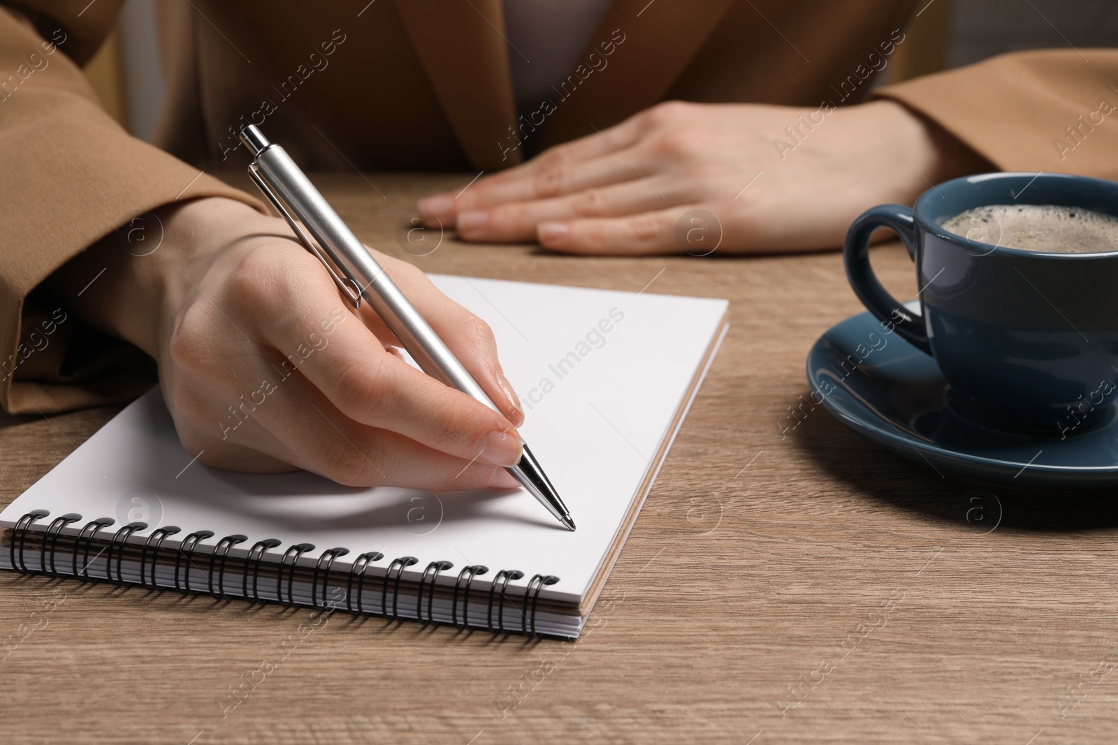 Photo of Woman writing in notebook at wooden table, closeup