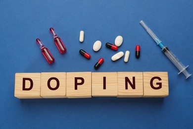 Photo of Wooden cubes with word Doping and drugs on blue background, flat lay