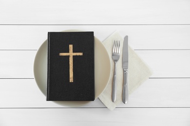 Photo of Plate with Bible and cutlery on white wooden table, flat lay. Lent season