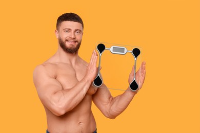 Photo of Portrait of happy athletic man with scales on orange background. Weight loss concept