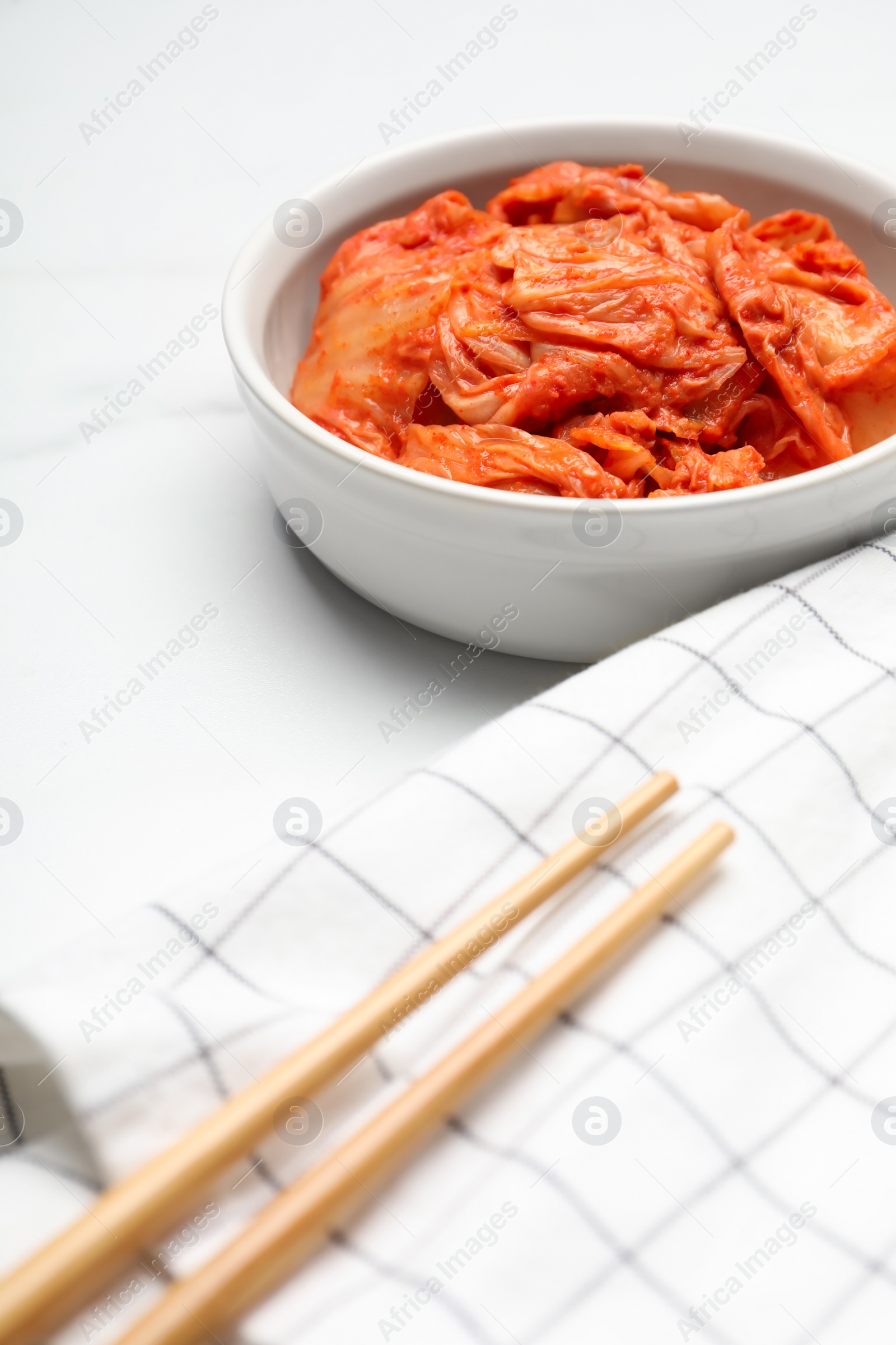 Photo of Bowl of spicy cabbage kimchi and chopsticks on white marble table