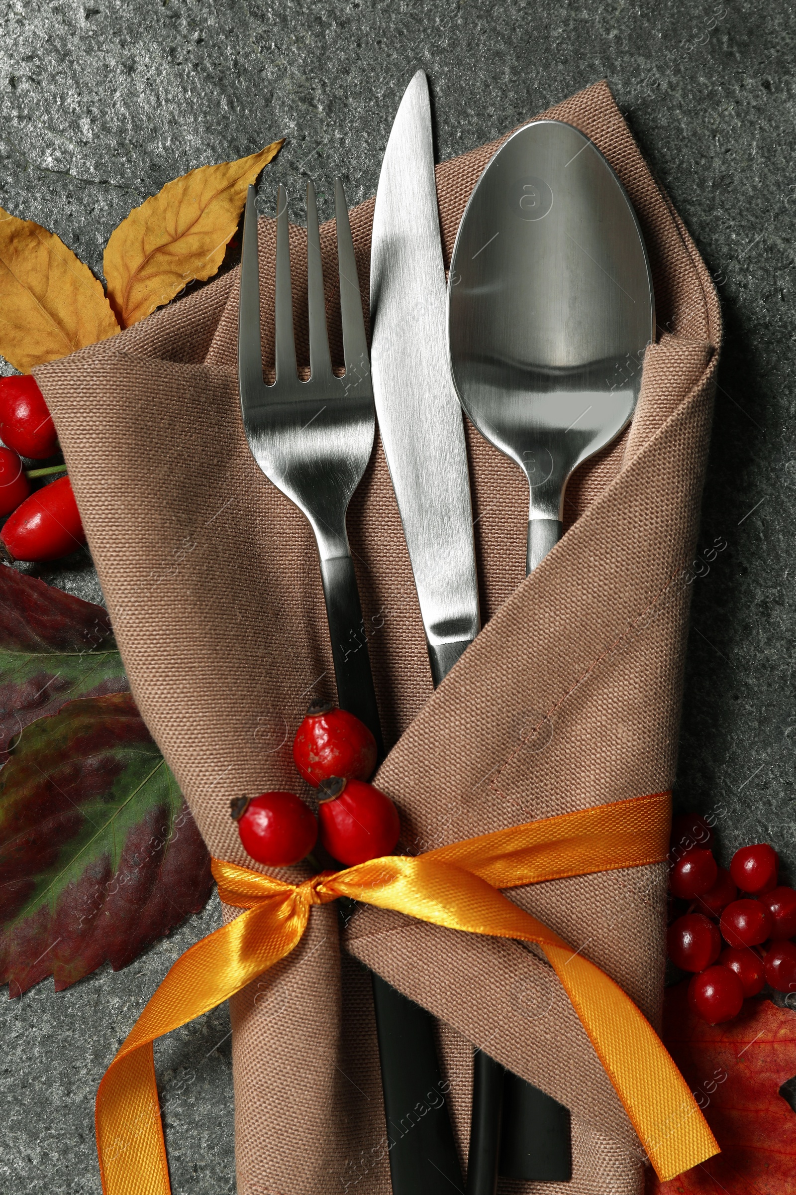 Photo of Thanksgiving table setting. Cutlery, napkin, autumn leaves and berries on grey background, flat lay