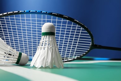 Photo of Feather badminton shuttlecocks and racket on green table against blue background, closeup