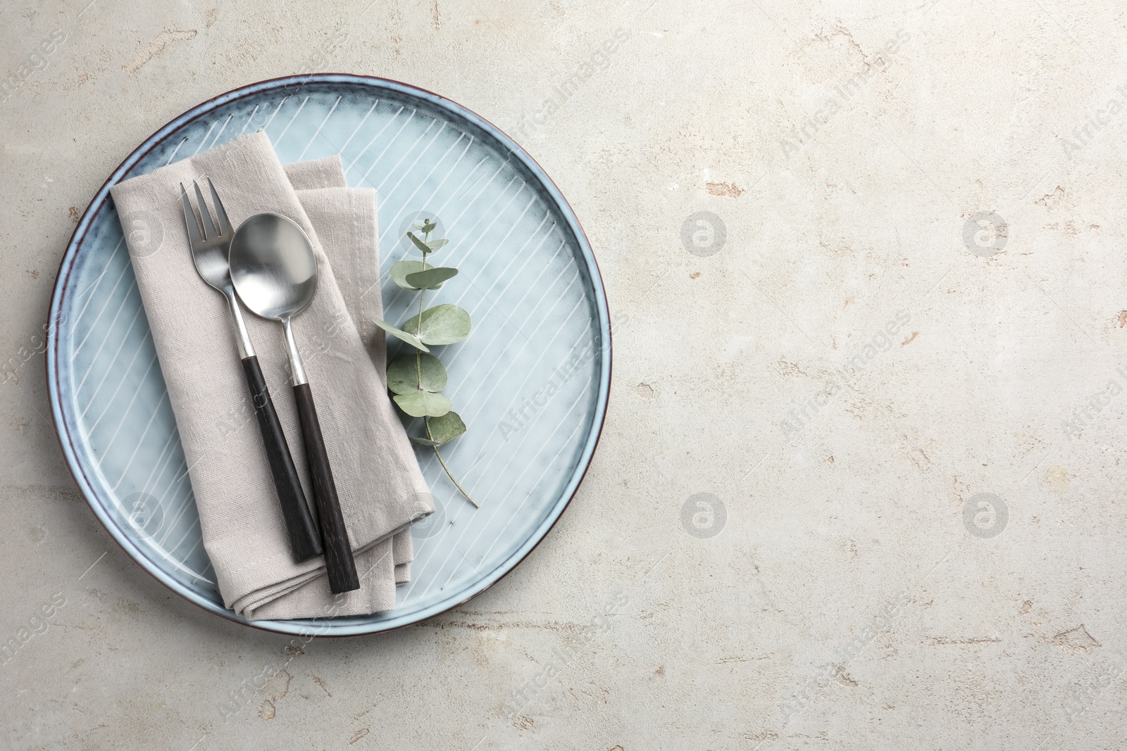 Photo of Stylish setting with cutlery, napkin, eucalyptus branch and plate on light grey table, top view. Space for text