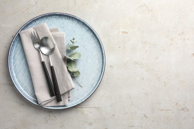 Stylish setting with cutlery, napkin, eucalyptus branch and plate on light grey table, top view. Space for text
