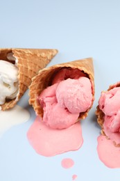Photo of Melted ice cream in wafer cones on light blue background, closeup