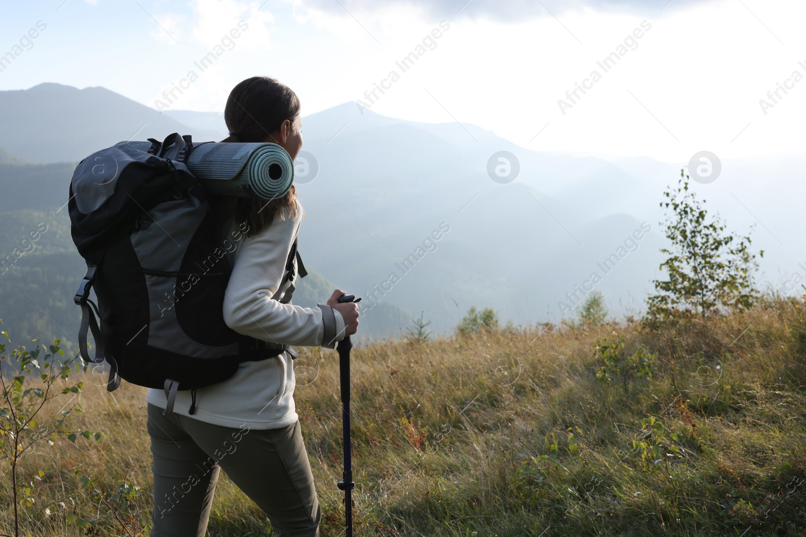 Photo of Tourist with backpack and trekking poles hiking through mountains, space for text