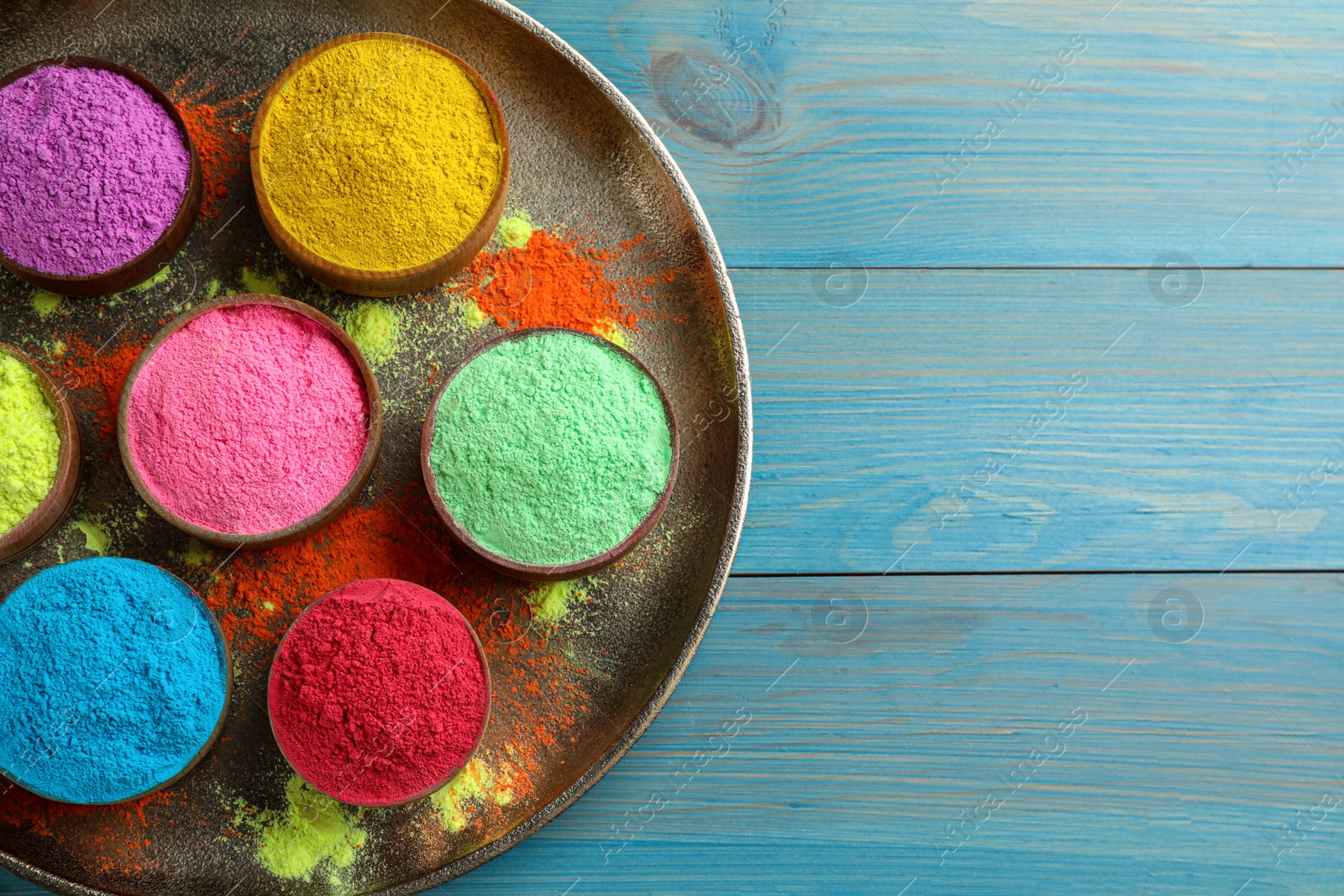 Photo of Colorful powder dyes on light blue wooden background, top view with space for text. Holi festival