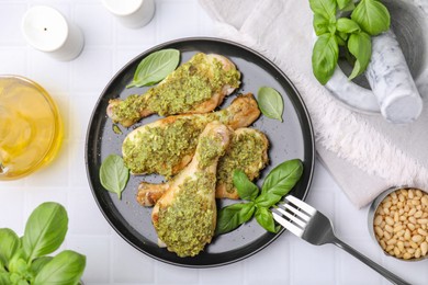 Delicious fried chicken drumsticks with pesto sauce, ingredients and fork on white table, flat lay