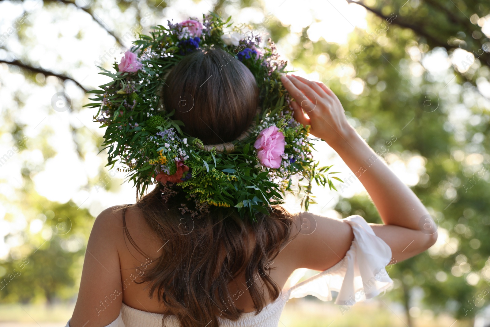 Photo of Young woman wearing wreath made of beautiful flowers outdoors on sunny day, back view