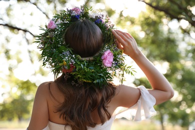 Young woman wearing wreath made of beautiful flowers outdoors on sunny day, back view