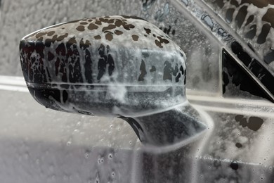 Photo of Automobile side-view mirror with cleaning foam at car wash, closeup