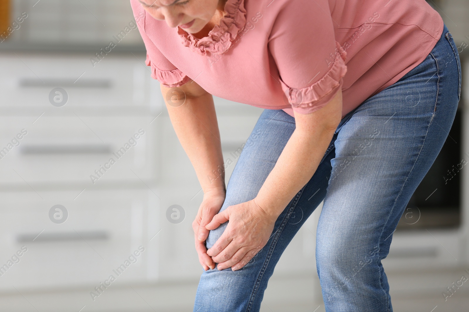 Photo of Senior woman suffering from knee pain in kitchen, closeup. Space for text