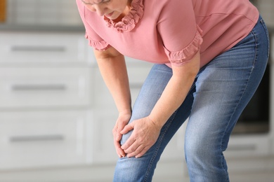 Senior woman suffering from knee pain in kitchen, closeup. Space for text
