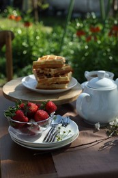 Photo of Beautiful spring flowers, freshly baked waffles and ripe strawberries on table served for tea drinking in garden