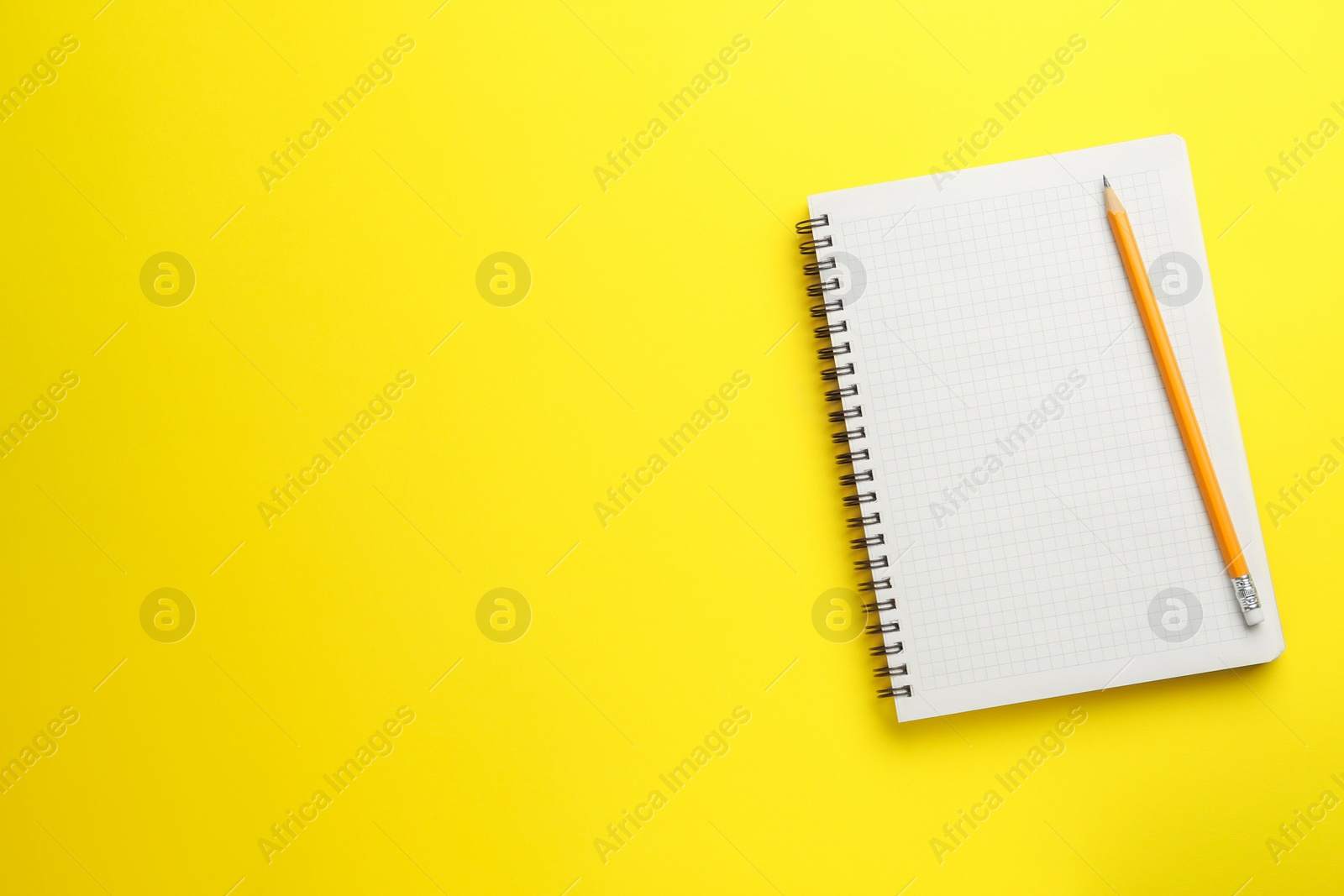 Photo of Notebook and pencil on yellow background, top view. Space for text