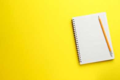 Photo of Notebook and pencil on yellow background, top view. Space for text