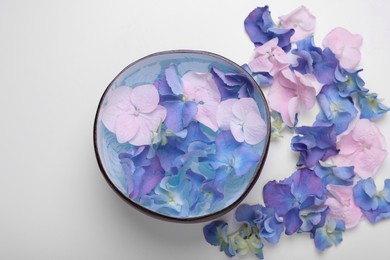 Spa composition. Aromatic water in bowl and flowers on white background, flat lay