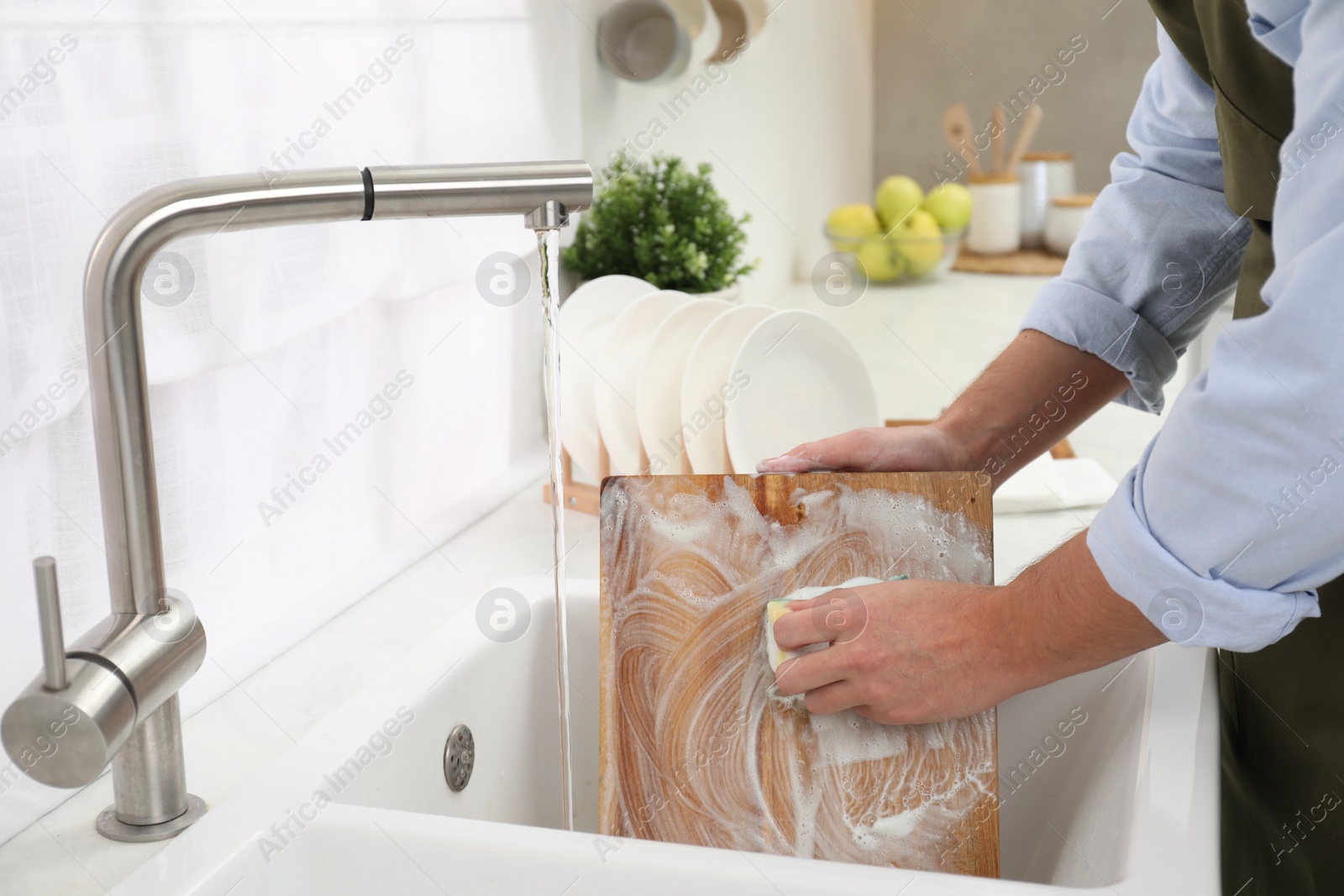 Photo of Man washing wooden cutting board in kitchen sink, closeup