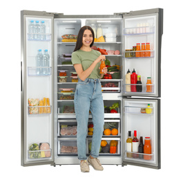 Young woman with bottle of juice near open refrigerator on white background