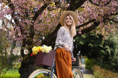 Photo of Beautiful young woman with bicycle and flowers in park on pleasant spring day
