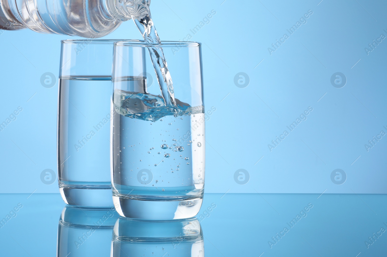 Photo of Pouring water from bottle into glass on light blue background. Space for text