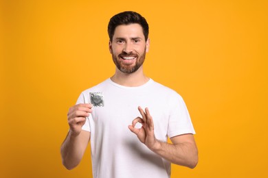 Photo of Happy man with condom showing ok gesture on yellow background. Safe sex