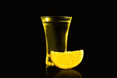 Shot glass of vodka with lemon slice on dark background