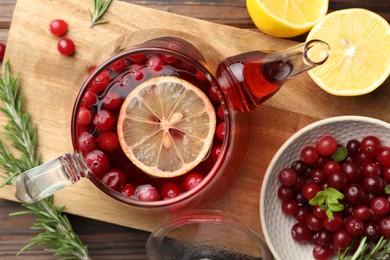 Photo of Tasty hot cranberry tea, lemon, rosemary and fresh berries on wooden table