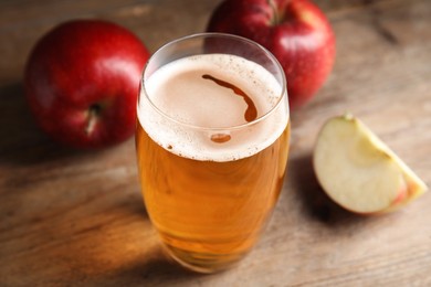 Glass of delicious cider and ripe red apples on wooden table, closeup