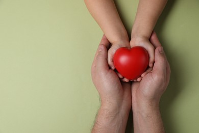 Father and his child holding red decorative heart on light green background, top view. Space for text