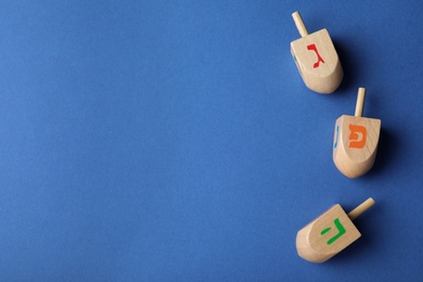 Photo of Hanukkah traditional dreidels with letters Gimel, Pe and He on blue background, flat lay. Space for text