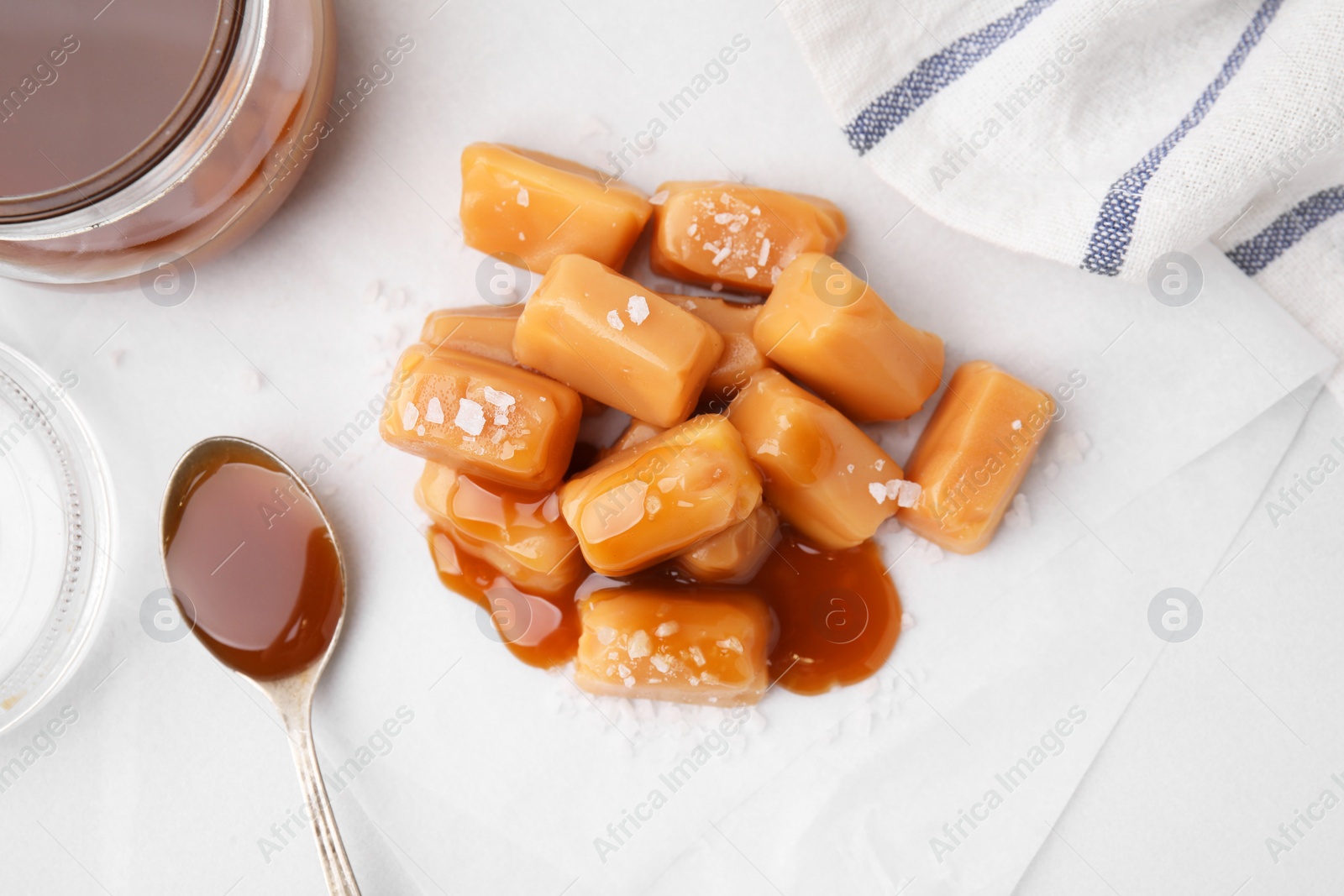 Photo of Yummy caramel candies and sea salt on white table, flat lay