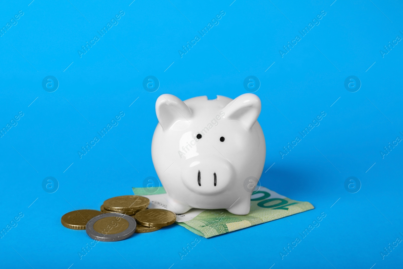 Photo of Ceramic piggy bank, euro banknote and coins on light blue background. Financial savings