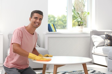 Man cleaning table with rag in living room