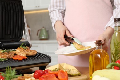 Woman cooking different products with electric grill at wooden table in kitchen, closeup