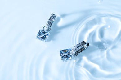 Photo of Luxury jewelry. Elegant earrings in water on light blue background