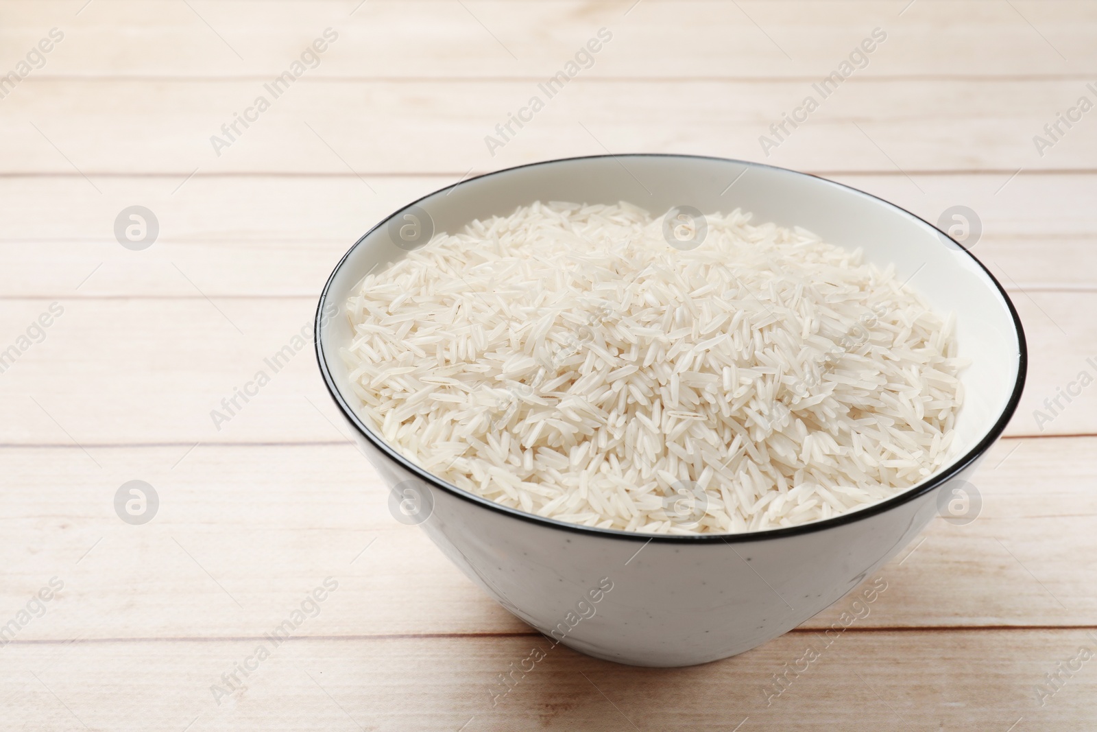 Photo of Raw basmati rice in bowl on white wooden table, space for text