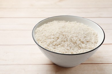 Photo of Raw basmati rice in bowl on white wooden table, space for text