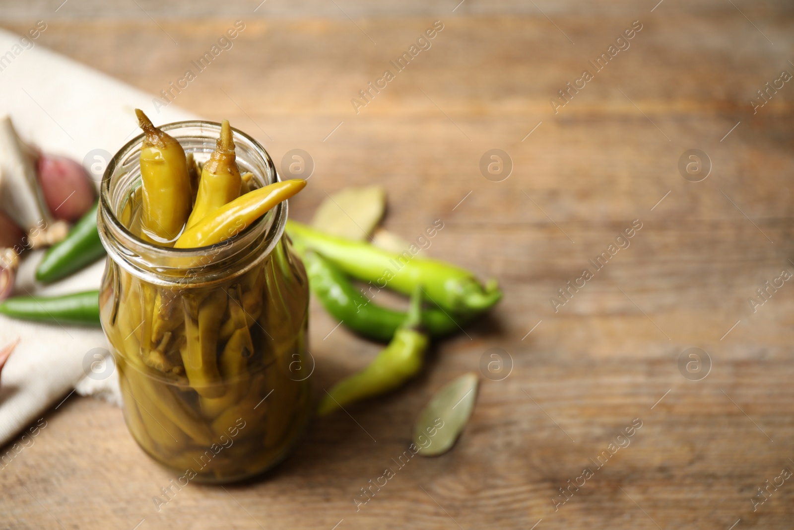 Photo of Glass jar with pickled peppers on wooden table. Space for text