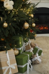 Photo of Many gift boxes under Christmas tree decorated with ornaments and festive lights in room