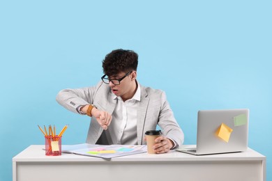 Photo of Emotional young man working at white table on light blue background. Deadline concept