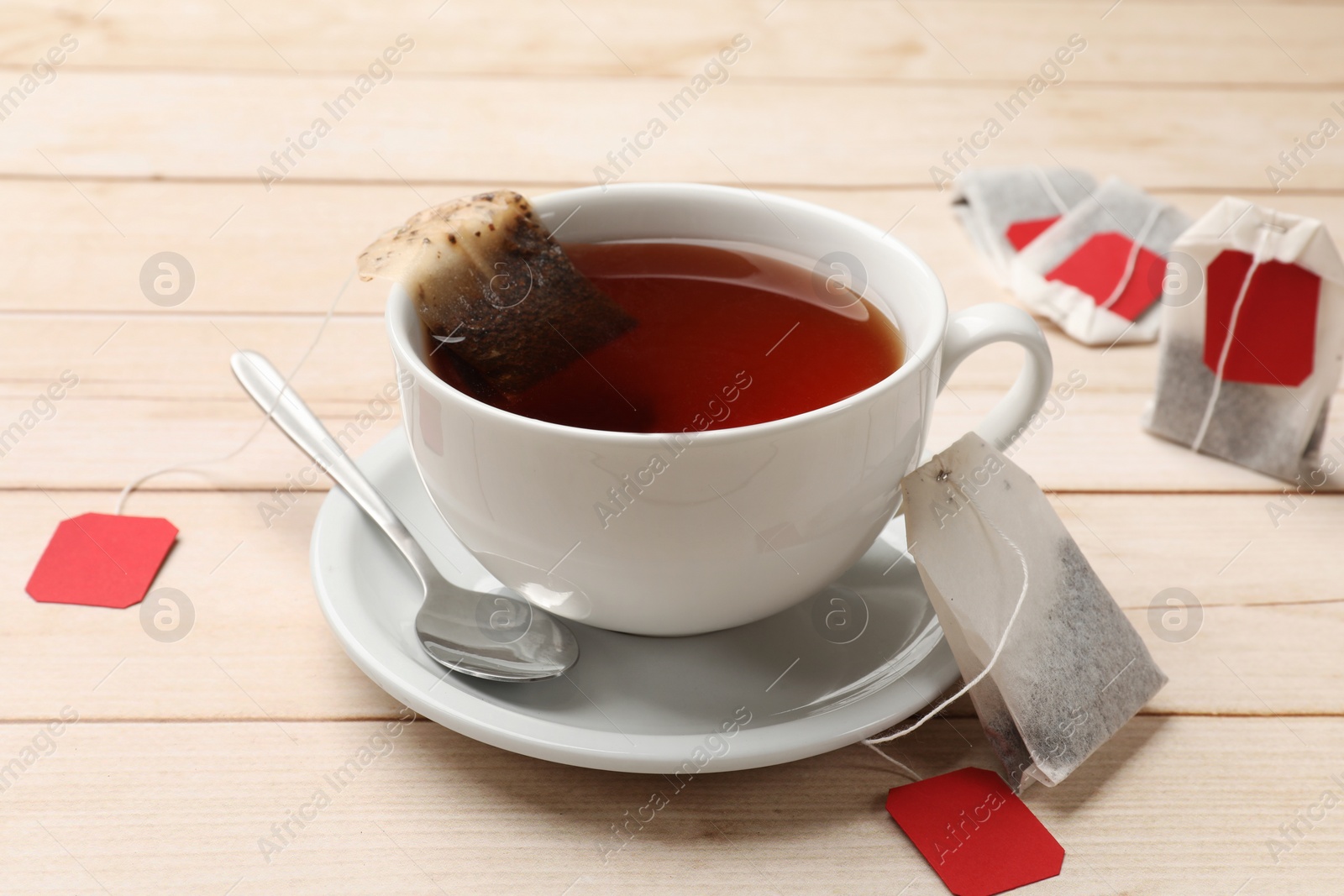 Photo of Tea bags, cup of hot beverage and spoon on light wooden table, closeup