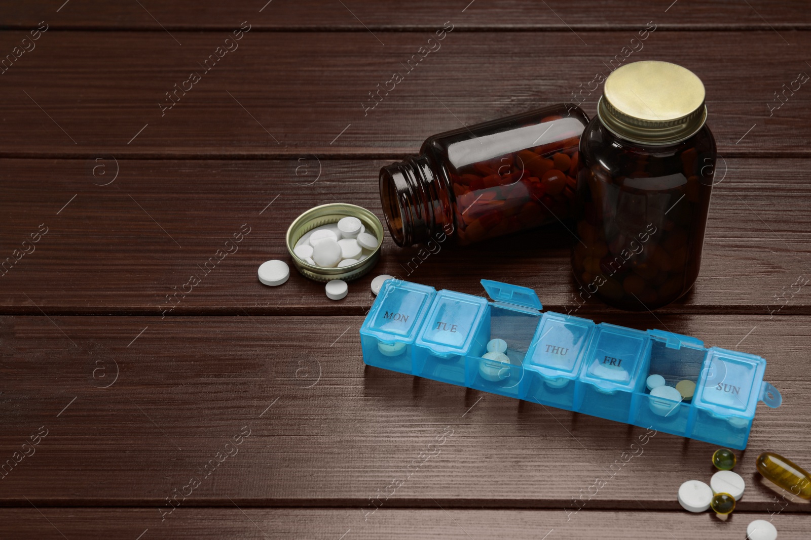 Photo of Weekly pill box and bottles with medicaments on wooden table. Space for text