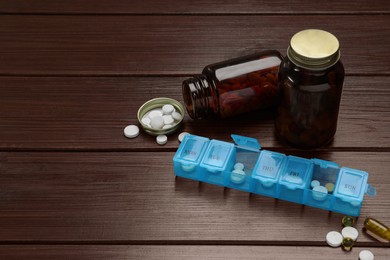 Photo of Weekly pill box and bottles with medicaments on wooden table. Space for text