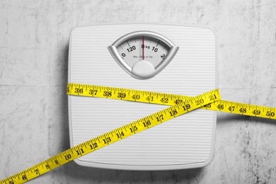 Photo of Scales and measuring tape on grey textured background, top view. Weight loss concept