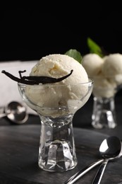 Photo of Tasty ice cream with vanilla pods in glass dessert bowl on black table